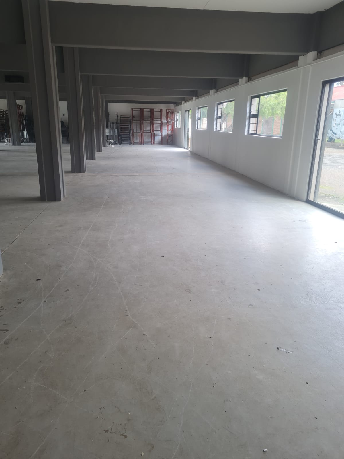 Empty industrial space with concrete floor, steel beams, and windows